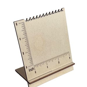 May include: A wooden earring display stand with a ruler printed on the side. The stand is made of light-colored wood and has a series of small notches along the top edge. The ruler is marked in inches, up to 3 inches.