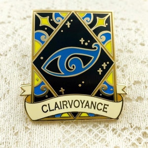 May include: Gold-toned enamel pin with a blue eye design and a banner that reads "Clairvoyance". The eye is surrounded by a black background with yellow and blue swirls.