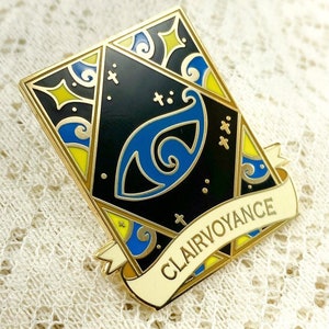 May include: Gold-toned enamel pin with a black background and a blue eye design. The pin features a white banner with the text "Clairvoyance" in yellow lettering.