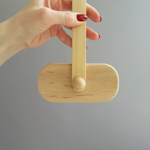 K&ouml;nnte beinhalten: Ein ovales Objekt aus Holz mit einem Holzgriff. Das Objekt h&auml;ngt am Griff und wird von einer Hand gehalten.