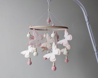 May include: A pink and white felt butterfly mobile with wooden beads and pink pom-poms hanging from a wooden ring.