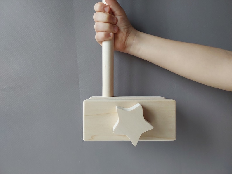 May include: A wooden toy hammer with a star-shaped head and a wooden handle. The hammer is painted in a natural wood color.