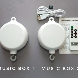 May include: Two white musical boxes with a hook for hanging. The boxes are labeled "Music Box 1" and "Music Box 2". A remote control with buttons for on/off, volume, and music selection is included.