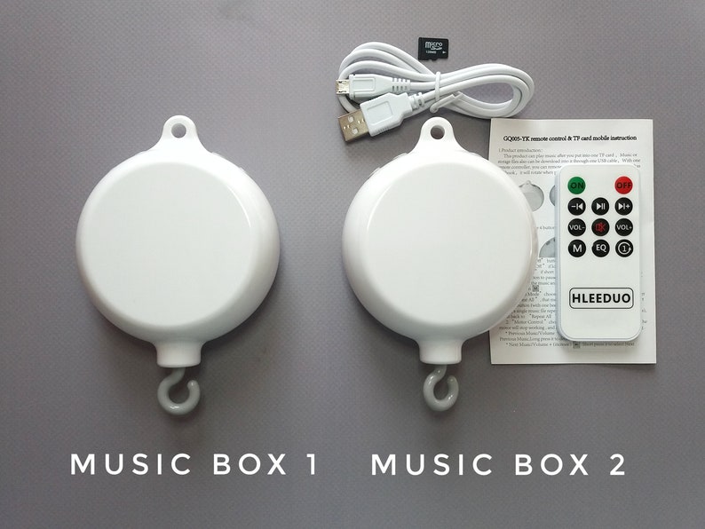 May include: Two white musical boxes with a hook for hanging. The boxes are labeled "Music Box 1" and "Music Box 2". A remote control with buttons for on/off, volume, and music selection is included.