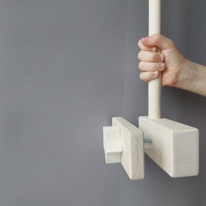 May include: A white wooden dowel rod with a knob on one end and a rectangular wooden block attached to the other end. The rod is attached to the block with a screw. The block has a smaller rectangular block attached to it with a screw.