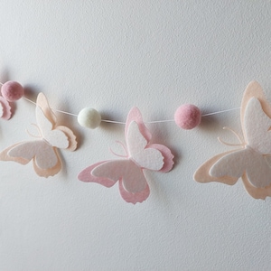 May include: A pink and white felt butterfly garland with white pom poms strung on a white string.