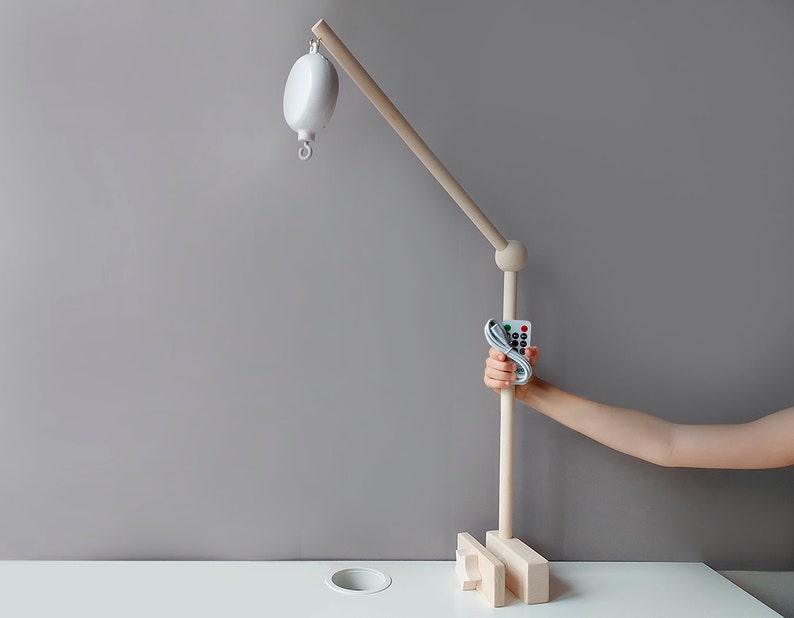 May include: A white wooden baby mobile with a remote control. The mobile has a white ball hanging from it and is mounted on a wooden stand. The remote control has buttons for different colors and speeds.