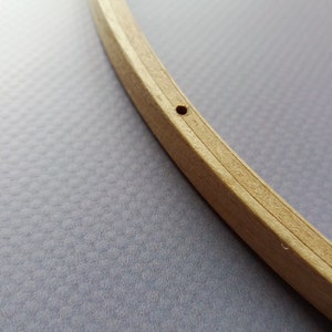 Op de afbeelding: Een close-up van een houten borduurring met een klein gat geboord in de bovenkant. De ring is gemaakt van twee stukken hout die aan elkaar worden gehouden door een metalen ring.