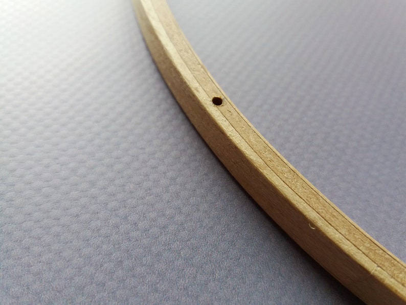 Op de afbeelding: Een close-up van een houten borduurring met een klein gat geboord in de bovenkant. De ring is gemaakt van twee stukken hout die aan elkaar worden gehouden door een metalen ring.