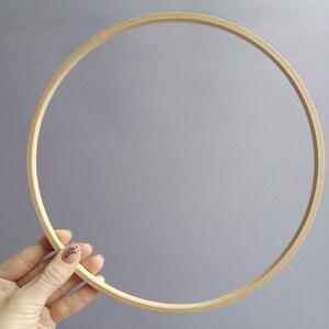 Op de afbeelding: Een ronde borduurring van natuurlijk hout met een glad oppervlak. De ring wordt in een hand gehouden, waardoor de grootte en vorm duidelijk worden.