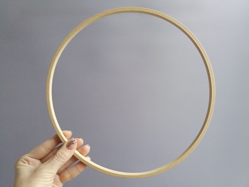 Op de afbeelding: Een ronde borduurring van natuurlijk hout met een glad oppervlak. De ring wordt in een hand gehouden, waardoor de grootte en vorm duidelijk worden.