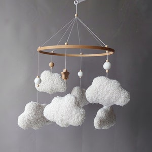 May include: A wooden baby mobile with white fluffy clouds and wooden beads hanging from a circular wooden frame. A small wooden star hangs in the centre.