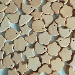 Könnte beinhalten: Eine Sammlung von Holzperlen in verschiedenen Formen, darunter Sterne, Vögel und Blumen. Die Perlen sind alle in natürlicher Holzfarbe und haben eine glatte, polierte Oberfläche.
