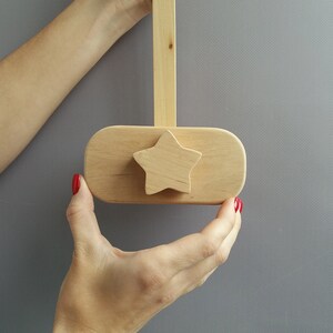 K&ouml;nnte beinhalten: Ein h&ouml;lzerner sternf&ouml;rmiger Knopf mit nat&uuml;rlicher Oberfl&auml;che. Der Knopf ist an einer Holzstange befestigt und wird von zwei H&auml;nden gehalten.