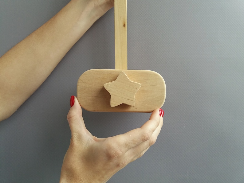 K&ouml;nnte beinhalten: Ein h&ouml;lzerner sternf&ouml;rmiger Knopf mit nat&uuml;rlicher Oberfl&auml;che. Der Knopf ist an einer Holzstange befestigt und wird von zwei H&auml;nden gehalten.