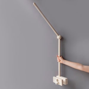 May include: A white wooden mobile arm with a round knob at the top and a rectangular base. The arm is attached to a wall and can be adjusted to different angles.