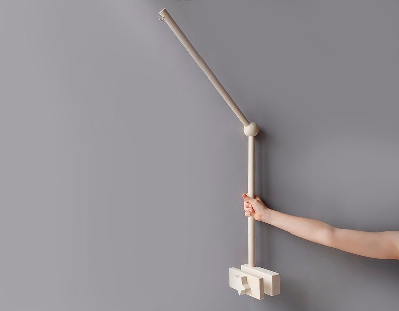 May include: A white wooden mobile arm with a round knob at the top and a rectangular base. The arm is attached to a wall and can be adjusted to different angles.