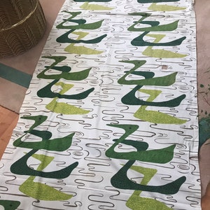 May include: A white fabric with a repeating pattern of green and brown abstract shapes. The shapes resemble stylised birds or swans.