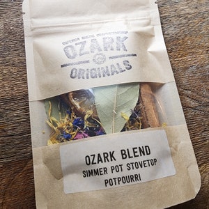 Könnte beinhalten: Ein brauner Papierbeutel mit einem durchsichtigen Fenster, das eine Mischung aus getrockneten Kräutern und Gewürzen zeigt. Der Beutel trägt ein Etikett mit der Aufschrift "Ozark Blend Simmer Pot Stovetop Potpourri".