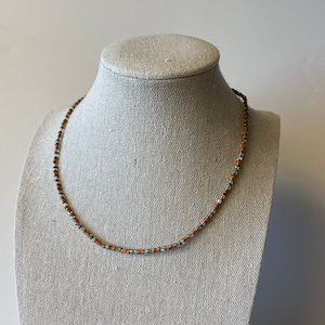 May include: A silver and orange beaded necklace on a white mannequin.
