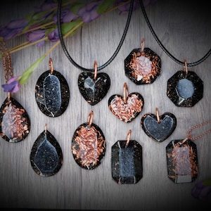 May include: A collection of 10 black and copper resin pendants with various shapes, including hearts, ovals, and octagons. The pendants are strung on black and copper chains.