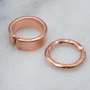 May include: Two copper jump rings, one with a smooth finish and the other with a hammered texture.
