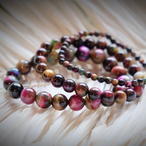 May include: A set of four bracelets made with iridescent tiger's eye beads in shades of brown, black, and pink. The beads are round and have a smooth, polished finish.