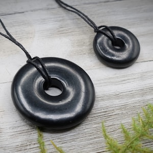 May include: Two black obsidian donut pendants on black cords. The larger pendant is about 2 inches in diameter and the smaller pendant is about 1 inch in diameter.