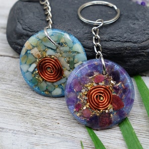 May include: Two round crystal keyrings with copper wire spirals. The keyring on the left is blue with white and green crystals. The keyring on the right is purple with pink and white crystals.
