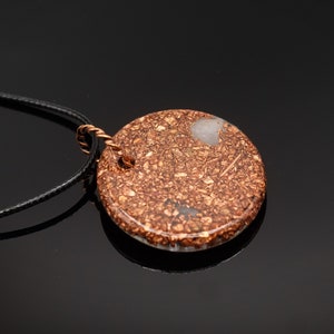 May include: A round copper and white pendant with a black cord necklace. The pendant has a speckled copper finish with white flecks.