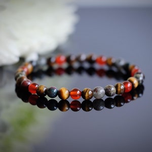 May include: A beaded bracelet with brown, red, and green stones. The bracelet is made of natural stones and is designed to be worn on the wrist.