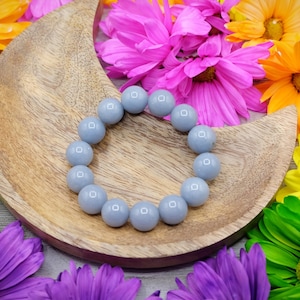 May include: A grey gemstone bracelet with round beads on a wooden crescent moon-shaped tray surrounded by colourful flowers.