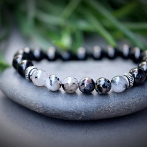 May include: A black and white beaded bracelet with silver accents. The bracelet is made of round beads and is resting on a gray stone.