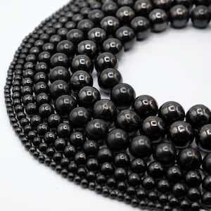 May include: Close-up of multiple strands of black, glossy beads of varying sizes. The beads are arranged in a curved pattern, showcasing their round shape and reflective surface. The background is plain white.