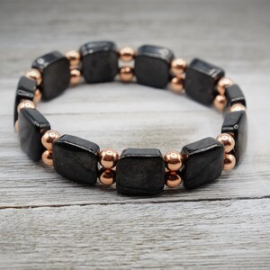 May include: Black gemstone bracelet with rose gold beads. The bracelet is made of square-shaped black stones and round rose gold beads.