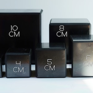 May include: Six black square boxes of different sizes, labelled with their dimensions in centimetres. The boxes are arranged in a row from largest to smallest, with the largest box measuring 10 cm and the smallest box measuring 3 cm.