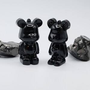 May include: Two black bear-shaped figurines with a glossy finish. The figurines are standing on a white surface.