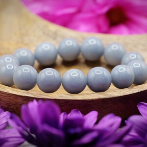 May include: A bracelet made of light blue round beads. The bracelet is on a wooden surface with purple flowers.