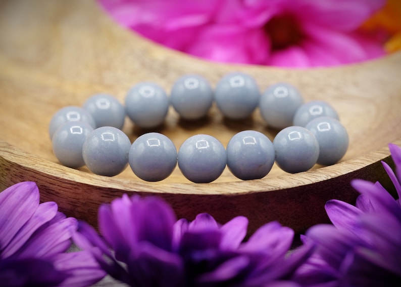 May include: A bracelet made of light blue round beads. The bracelet is on a wooden surface with purple flowers.