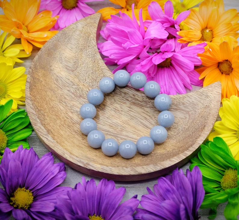 May include: A grey gemstone bracelet with round beads on a wooden crescent moon-shaped tray surrounded by colourful flowers.