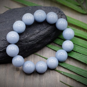 May include: A light blue gemstone bracelet with round beads. The bracelet is on a dark grey stone and green leaves.