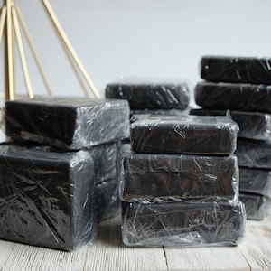 May include: A stack of black soap bars wrapped in clear plastic. The bars are arranged in a pyramid shape.