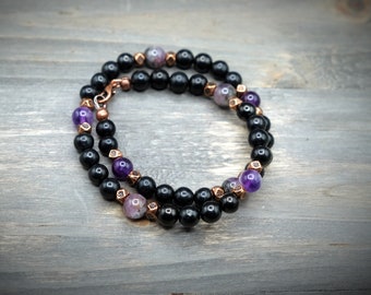 May include: A black and purple beaded bracelet with copper accents. The bracelet is made with black onyx, amethyst, and copper beads.