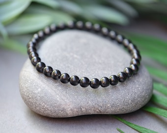 May include: A black beaded bracelet made of round, smooth stones. The bracelet is lying on a gray rock.