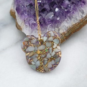 May include: A gold chain necklace with a heart-shaped pendant filled with small green and white stones and gold glitter.
