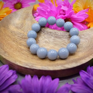 May include: A grey gemstone bracelet with round beads on a wooden crescent moon-shaped dish. The dish is surrounded by colourful flowers.