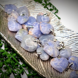 May include: A collection of blue and white heart-shaped pendants made of polished blue lace agate. The pendants have silver jump rings and are displayed on a silver tray.