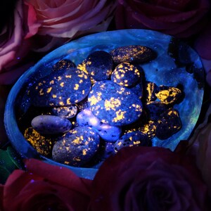 May include: A collection of blue and yellow speckled stones in a blue bowl, surrounded by pink roses.