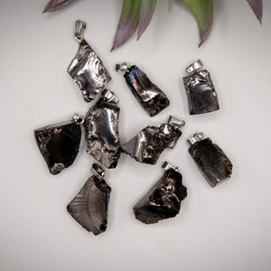 May include: A collection of eight black obsidian pendants with silver bail settings. The pendants are all different shapes and sizes, and they have a rough, natural look.