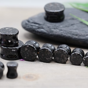 May include: A set of black and white speckled ear gauges in various sizes. The gauges are made of a smooth, polished material and have a slightly rounded shape.
